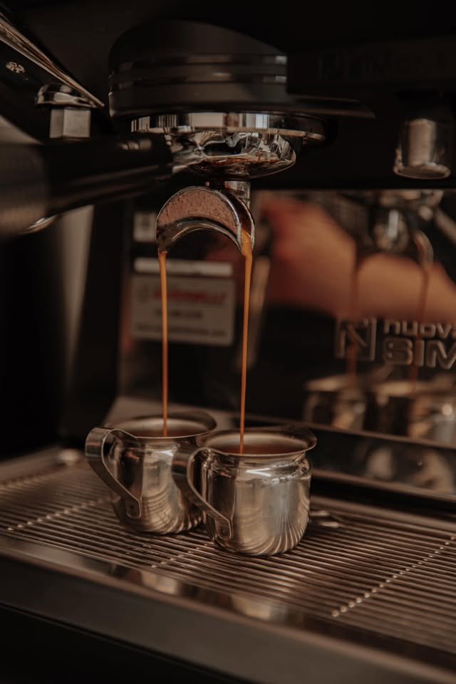 A double espresso pulling into two steel pitchers on the machine