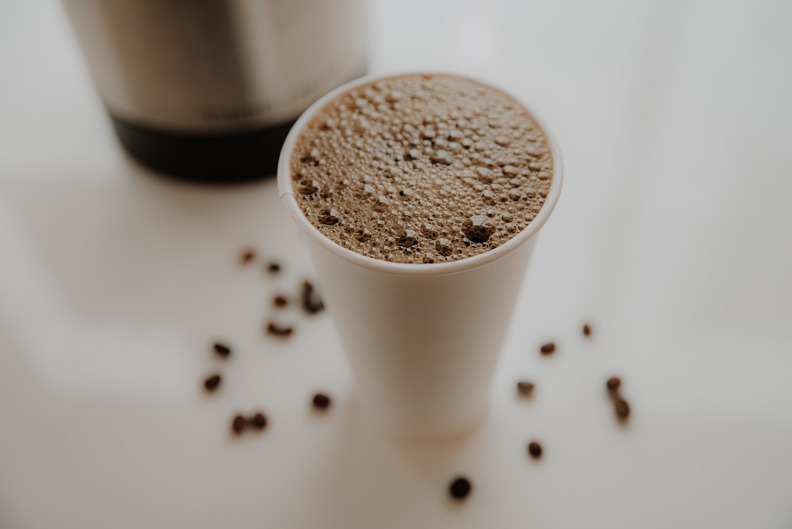 A blended frozen coffee drink with coffee beans scattered on a white surface
