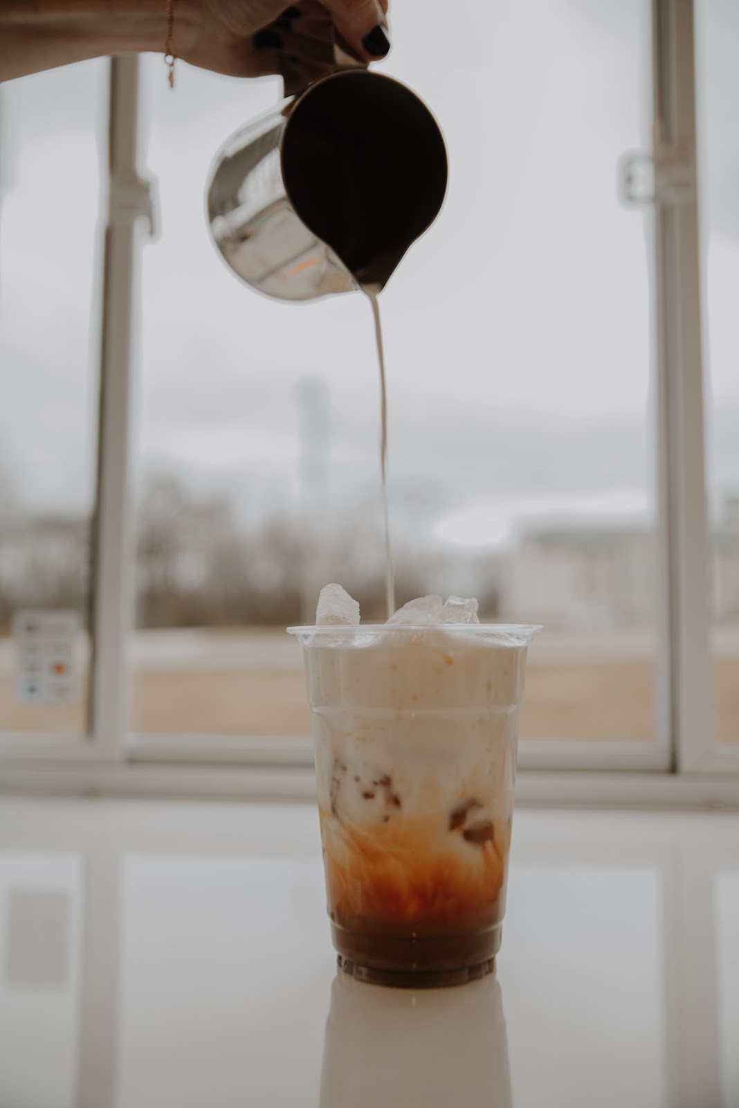 Milk being poured into an iced latte in front of a window on Monument Square