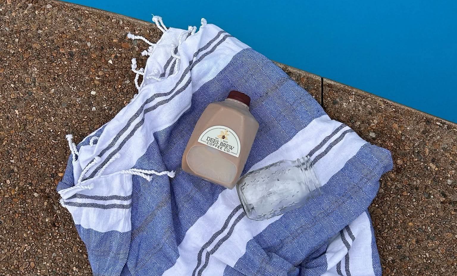A 32 ounce Dees Brew jug of iced coffee and an empty mason jar on a striped towel